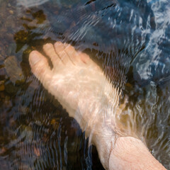 Close up human foot while stand in rapid water stream, relax in shallow creek, day off in nature,...