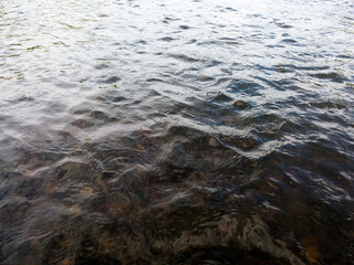 Wavy surface of water on shallow rapid stream with colorful gravel at bottom, running water in creek, intimate landscape