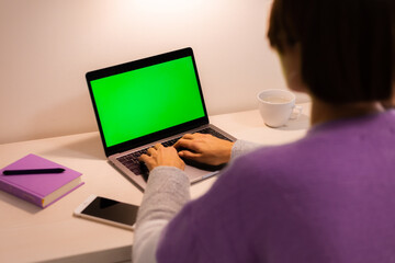 Fototapeta na wymiar Woman at home in bedroom watching green screen on laptop on table, notebook and pen lying near by. 