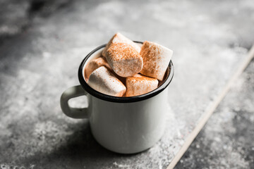 Vintage white metal cup with hot chocolate and marshmallow on the rustic background. Hygge winter evening. Selective focus. Shallow depth of field.