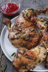Grilled chicken legs in a white round plate on a wooden table. Vertical image