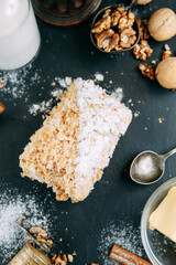 Napoleon cake with ingredients on a black stone Board. Napoleon cake with powdered sugar close-up.