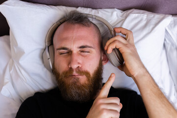Happy caucasian man on bed wearing headphone listen enjoy his favorite music, resting alone, dancing.  
