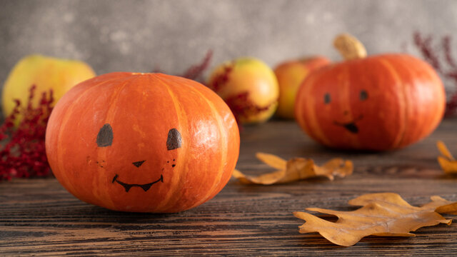 Halloween pumpkins with painted faces on a wooden table with autumn leaves. Halloween background. Space for text.
