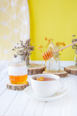 Glass cup of tea with linden in natural organic herbs and a jar of honey on a white wooden table.