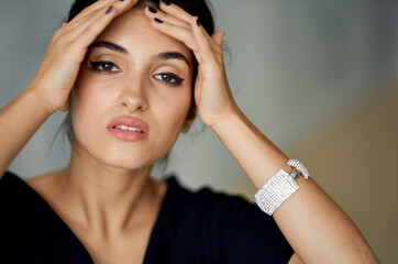 Fototapeta premium beautiful woman model touches her face with her hands on a gray background and evening dress decoration on her hand