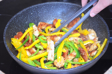 Close up of colorful green and yellow sliced bell peppers and pieces of chicken meat in black pan...
