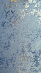 Ice and frost on the window. Pale blue winter wallpaper for a mobile phone. Frozen water crystal pattern, similar to the spectacular leaves of fantastic plants, shining like gems. Vertical background