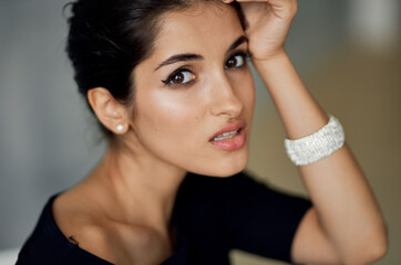 Obraz premium beautiful Lydia With evening make-up in a black dress sits indoors on a chair