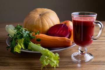 Still life with glass of freshly squeezed vegetable juice and plate with all kinds of vegetables.