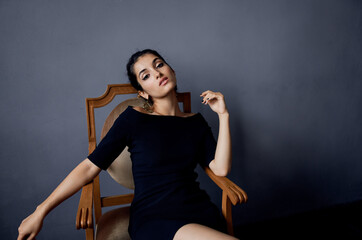 elegant woman in black dress sits on wooden chair in gray room