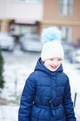 a girl in a blue jacket and a white hat is playing in a snowy yard