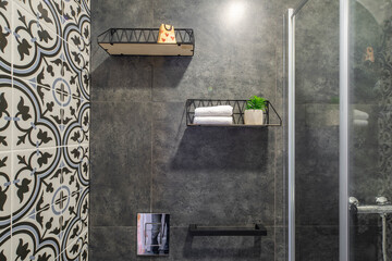 Modern interior of bathroom. Shower cabin. Grey tile. Shelves with towels and decor.