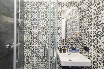 Modern interior of bathroom. Shower cabin. White sink and mirror. Patterned tile.