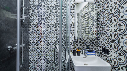 Modern interior of bathroom. Shower cabin. White sink and mirror. Patterned tile.