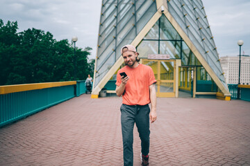 Positive young man using phone strolling in city