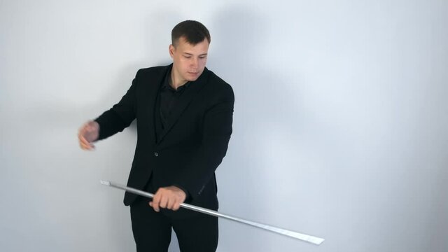 Illusionist is doing magic trick in slow motion. Magician man in black suit is showing trick doing metal stick from headscarf. Concept of performances, entertainments, shows and circus.