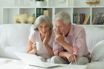 Surprised senior couple with laptop at home