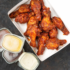 Takeaway box of crispy grilled chicken legs with a spicy marinade served with a hot chili dipping sauce, close up view