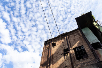 Abandoned industrial building, dirty brick exterior, broken out windows, green corrugated fiberglass against blue sky and clouds copy space, horizontal aspect
