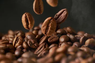  Close up of roasted coffee beans on a black smokey background. The grains fall from above in a group. © CreateLab