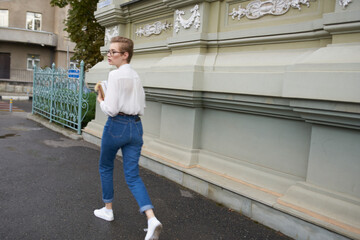 young woman in jeans and a shirt with a book in her hands near the building exterior education