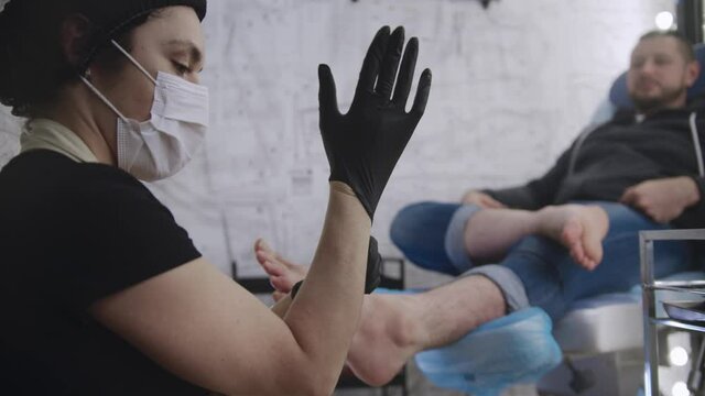 A man having a pedicure procedure - the master putting on a black glove