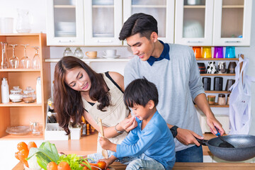 The cute boy and beautiful parents are cooking and smiling while happily cooking in the kitchen at home.