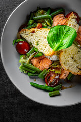 Green Bean Salad with Boiled Eggs, Salmon, Tomatoes and Arugula in a bowl on Dark grey black slate background