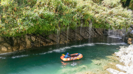 man rafting in water, natural landscape, green grass, flowing waterfall, cascade. man in boots
