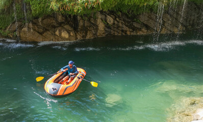 man rafting in water, natural landscape, green grass, flowing waterfall, cascade. man in boots
