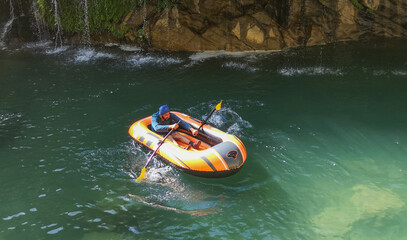 man rafting in water, natural landscape, green grass, flowing waterfall, cascade. man in boots
