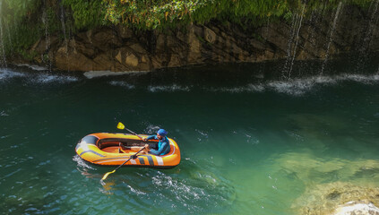 man rafting in water, natural landscape, green grass, flowing waterfall, cascade. man in boots
