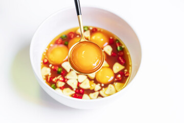 Pickled eggs yolk in fish sauce with chili pepper and garlic sliced in white bowl isolated on white background.