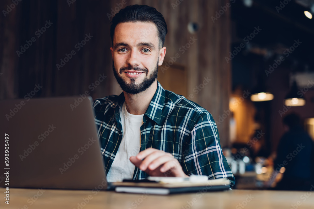 Poster portrait of happy caucasian man smiling at camera while doing web project via laptop application, su