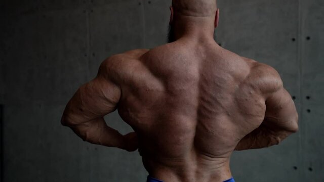 male bodybuilder is demonstrating muscles of back and arms, details of naked male body
