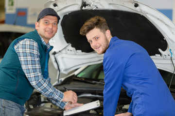 portrait of mechanic and apprentice by car with open hood