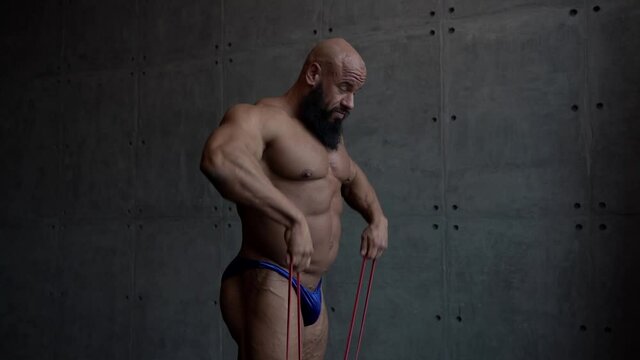 bearded bodybuilder dressed only blue panties is doing exercises for muscles, stretching rubber bands