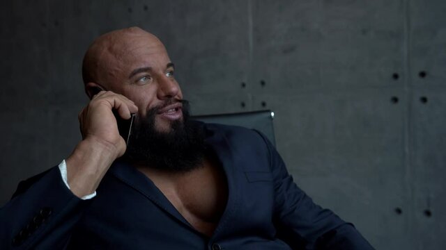 handsome bodybuilder is communicating by cell phone in office, sexy muscular man dressed jacket