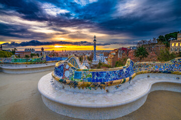 Beautiful sunrise in Barcelona seen from Park Guell. Park was built from 1900 to 1914 and was officially opened as a public park in 1926. In 1984, UNESCO declared the park a World Heritage Site - obrazy, fototapety, plakaty
