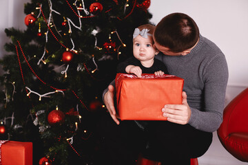 little girl unpacking gift with dad near Christmas tree.Happy girl unpacks holidays gift box. Happy lovely family