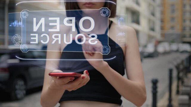 Unrecognizable young adult woman standing on the street interacts HUD hologram with text Open source. Girl in black clothes uses technology of the future mobile screen