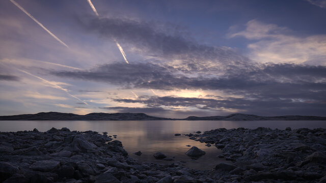 Peaceful lake scene at dusk with a cloudy sky reflecting in the still water. A calm, tranquil and serene, natural landscape.  
