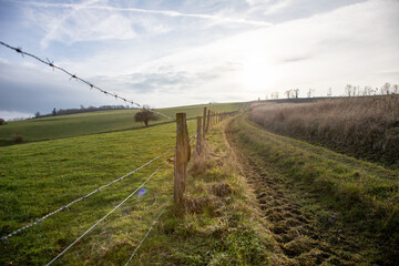 Hiking trail along fields and pastures, barbed wire fence separating a pasture.