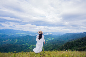 Fototapeta premium rear of happy woman wear white dress on top mountain looking view with mist and cloud at morning light Soft focus.