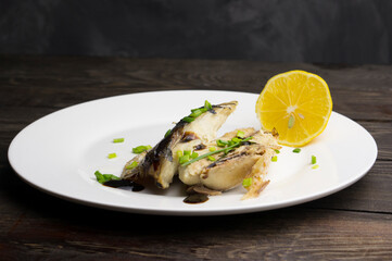 Grilled mackerel in a plate with herbs, lemon and sauce.