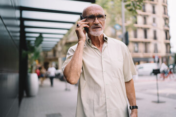 Serious male tourist in optical spectacles for provide eyes correction making international smartphone conversation in roaming, puzzled Caucasian man in classic glasses have consultancy call