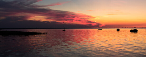 Beautiful sunset with reflexion on calm sea with silhouettes of small boats - Panorama