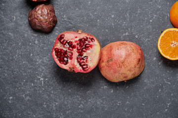 Close up of colourful pomegranate with orange on a dark grey stone background.