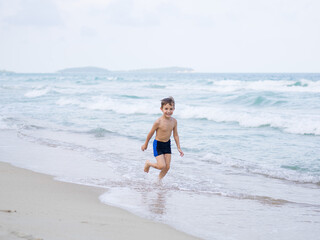 Happy boy runs along the beach against the background of the sea